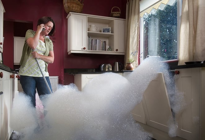 woman on phone with maintenance emergencies services in kitchen, dishwasher flooding woman on phone with maintenance emergencies services in kitchen, dishwasher flooding
