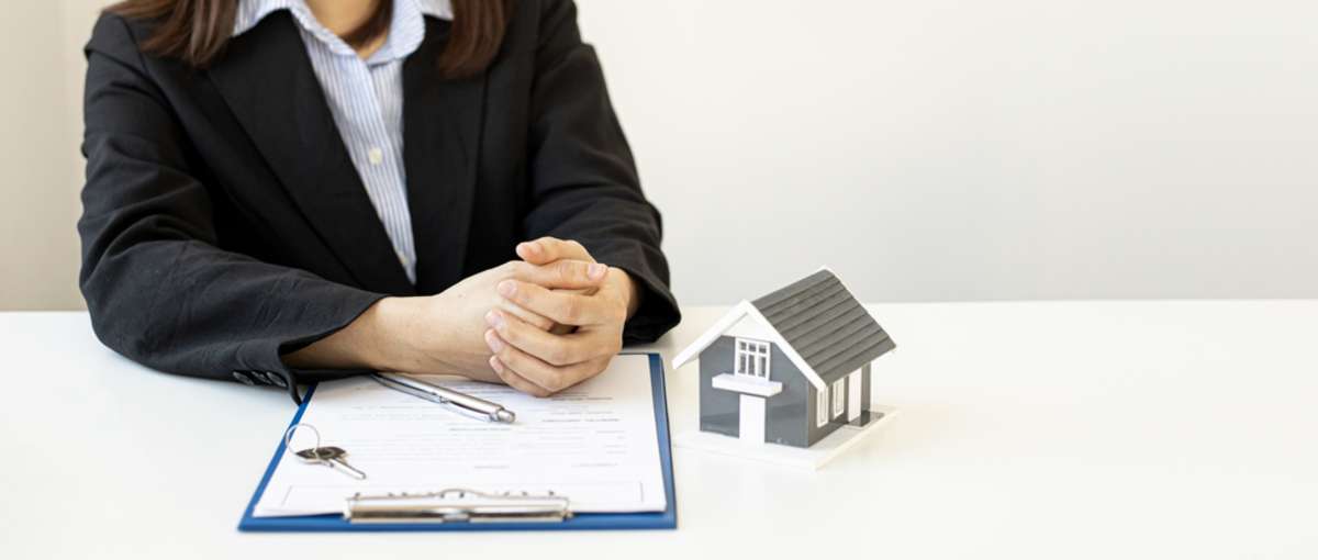 A professional sitting with a clipboard, keys, and a model of a house, property management concept